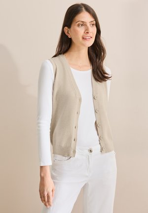 Beige gestrickt Weste mit V-Ausschnitt und Knopfverschluss, kombiniert mit einem weißen Langarmtop und weißen Hosen, glatte Textur, lässiges Design.