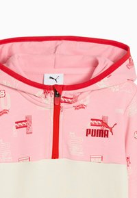 PUMA kapuce rozā un krēma krāsā, ar sarkanu rāvējslēdzēju, izšūtu logo un atkārtotām grafiskajām zīmējumiem. Mīksts kokvilnas audums.