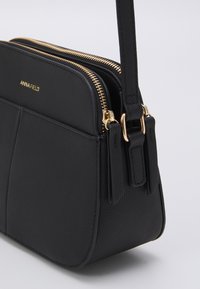 Borsa a tracolla in pelle nera con due scomparti con zip, dettagli in hardware dorato e finitura texturizzata. Compatta, con tracolla regolabile.