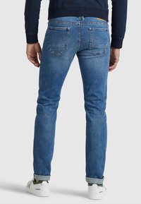 Jeans in denim blu aderenti con una consistenza morbida, cinque tasche e una leggera scoloritura. Abbinati a risvolti e sneakers bianche con dettagli verdi.