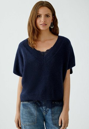 Navy blue, short-sleeve sweater with a v-neck and textured finish; features a lace accent at the neckline, paired with denim bottoms.
