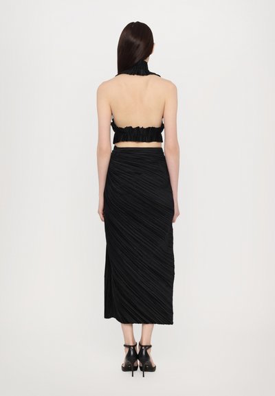 Čierny dvojdielny outfit obsahujúci bezrámčekový cropped top s volánmi a dlhú sukňu po zem s skrútenou, plisovanou textúrou.