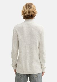 Hellgrauer, gerippter Pullover mit hohem Kragen. Verfügt über eine sprenkelte Textur und lange Ärmel. Getragen über lässigen, weit geschnittenen Jeans.