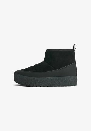 Black ankle boot with suede and rubber materials, featuring a textured platform sole and a pull tab at the back for easy wear.