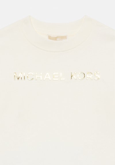 T-shirt creme da Michael Kors com gola redonda e texto dourado brilhante "MICHAEL KORS" centrado no peito.