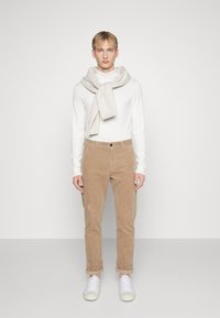 Suéter de cuello alto de manga larga blanco, bufanda beige clara drapeada alrededor del cuello, pantalones de pana color beige claro con los puños enrollados y zapatillas blancas. Paleta simple y neutral.