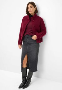 Giacca in misto lana bordeaux con colletto arrotondato e bottoni frontali, abbinata a una gonna in denim scuro lunghezza ginocchio con spacco frontale e stivali neri fino al ginocchio.