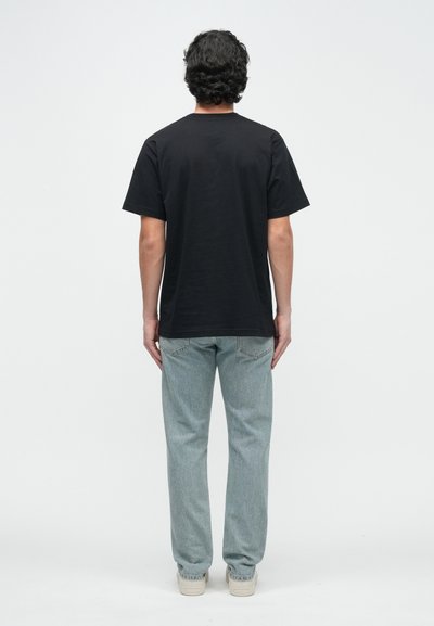 Juoda medvilninė trumpomis rankovėmis marškinėliai, laisvo stiliaus, su apvalia kaklo iškirpte, derinami su šviesiai mėlynais džinsais ir baltais sportbačiais.