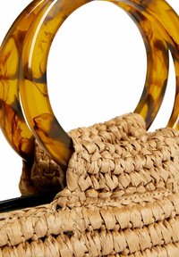 Torebka wpleciona z trawy, z dużymi uchwytami z żywicy w kolorze skorupy żółwia oraz teksturowanym, naturalnym wykończeniem, z widocznymi detalami szycia.