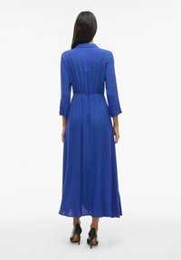 Dlhé modré šaty so stiahnutým pásom, rukávmi po tri štvrtiny a golierom. Vyrobené z ľahkej látky, siahajúce po polovicu teľa.