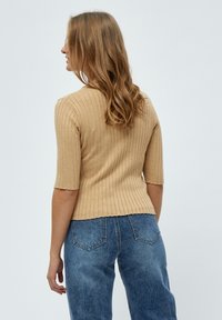 Top en tricot côtelé beige à manches courtes, design ajusté et ourlet court. Associé à un jean bleu taille haute.