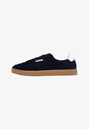 Baskets en daim bleu marine avec des accents blancs et une semelle en caoutchouc texturé couleur tan. Elles présentent une étiquette de marque sur le côté et des détails perforés.