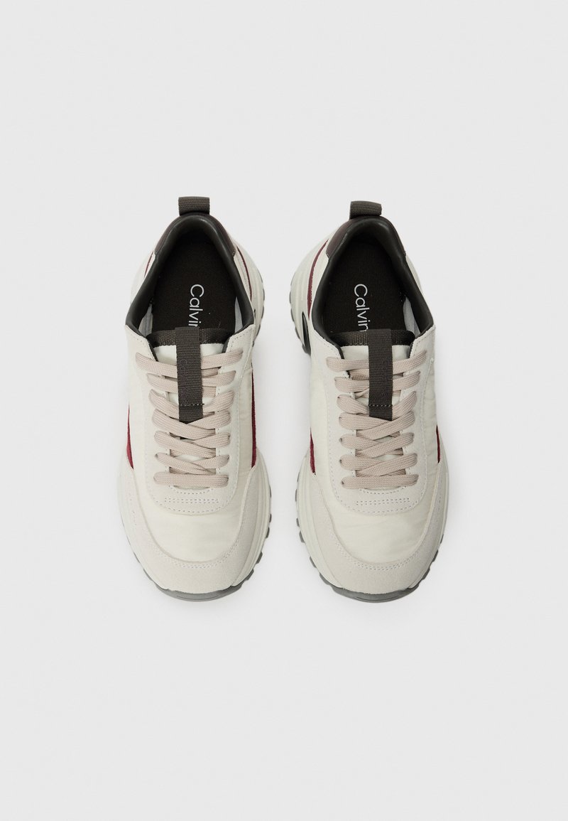 Zapatillas con una parte superior de un beige claro, acentos en burdeos y suela de goma gris. Las características incluyen un diseño con cordones y una lengüeta para facilitar el uso.