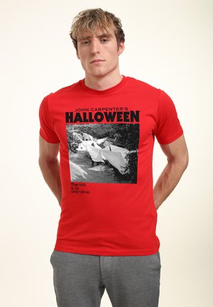 Rotes Baumwoll-T-Shirt mit einem Grafikdruck von "Halloween" von John Carpenter, mit schwarzem Text und einem Schwarz-Weiß-Bild. Kurze Ärmel.
