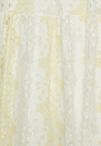 Spitzenstoff in hellgelb und weiß mit floralen Mustern. Das Design umfasst strukturierte Details, die ein mehrschichtiges Aussehen erzeugen.
