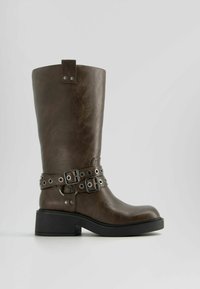 Hnědé kožené vysoké boty po kolena s blokovým podpatkem, detailem dvojité přezky a kovovými akcenty. Hladká textura s mírně opotřebovaným vzhledem.