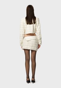 Witte textuur cropjack met een bijpassende rok, visnetpanty's en zwarte hakken, met een stijlvolle, minimalistische uitstraling.
