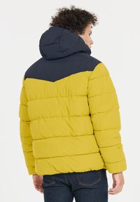 Puffjacka med en gul kropp och marinblå huva, med horisontell quiltning, elastiska ärmslut och en avslappnad passform.