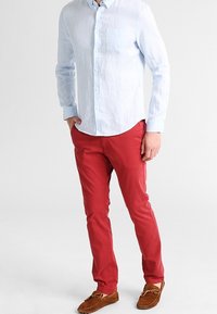 Ljusblå linneskjorta med långa ärmar och bröstficka, parat med smala röda bomullsbyxor och bruna mockaskor.