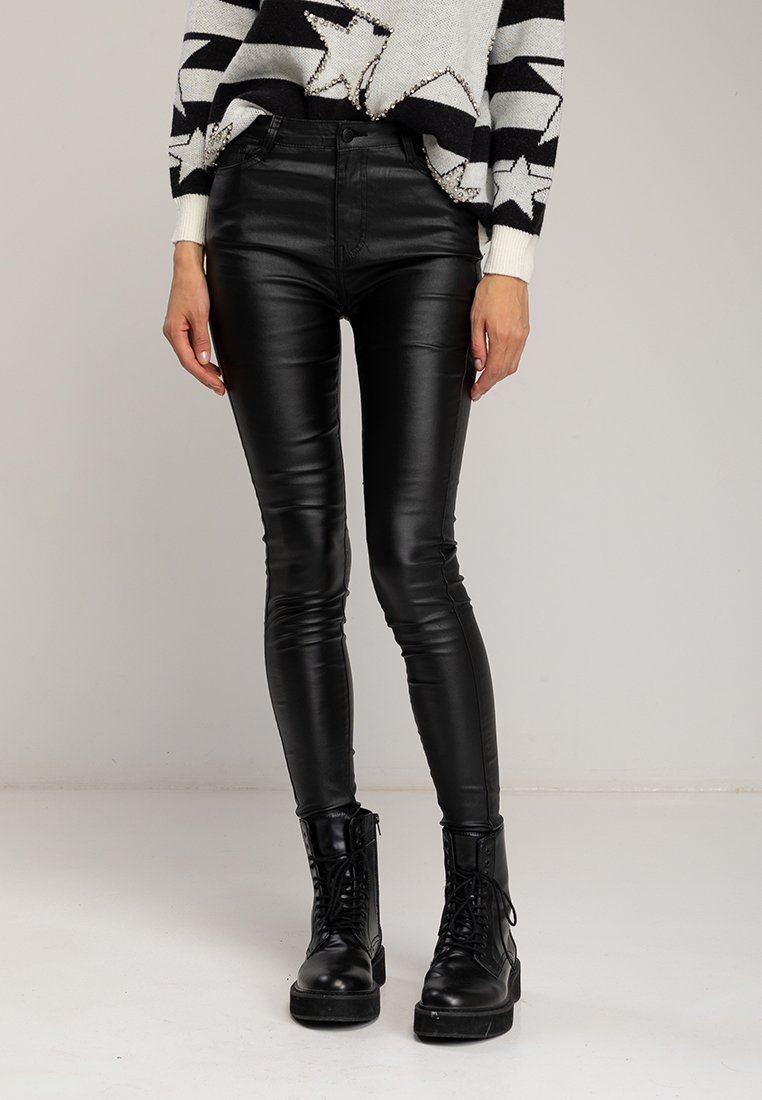 Zwarte nep leren skinny broek met hoge taille, voorzien van een glanzende afwerking en minimale stikdetails. Gecombineerd met stevige zwarte laarzen.
