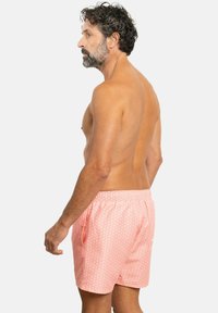 Bañadores de hombre en color rosa con un patrón floral en blanco, cinturilla elástica, bolsillos laterales y un detalle de bolsillo en la parte trasera.