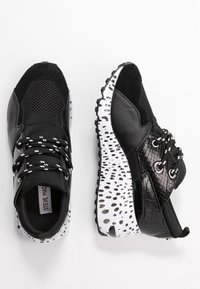 Sneakers da donna in bianco e nero con rete, materiale sintetico e suola con stampa animale, allacciati con lacci a fantasia bianco e nero.