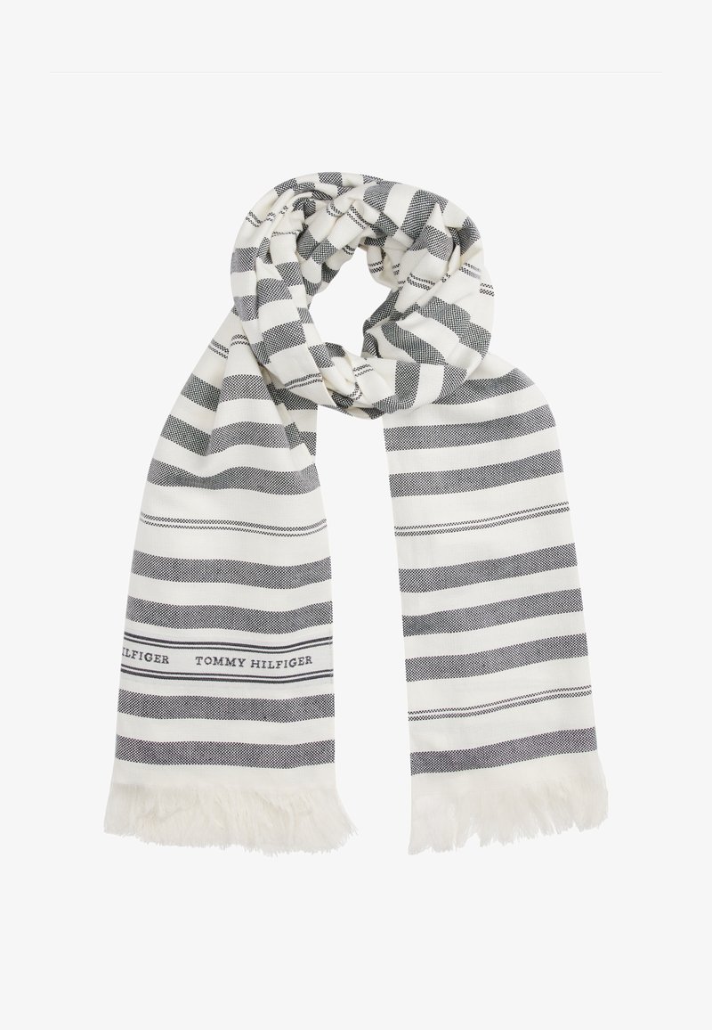 Λευκό και ναυτικό κασκόλ με ρίγες, κατασκευασμένο από μαλακό ύφασμα, με φούντες στις άκρες και μια επωνυμία που λέει "TOMMY HILFIGER" από τη μία πλευρά.