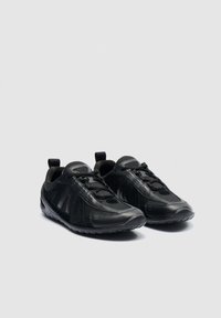 Par črnih športnih superg z mrežastimi in sintetičnimi prekrivnimi materiali, vezalkami in teksturiranimi gumijastimi podplati na nevtralnem ozadju.