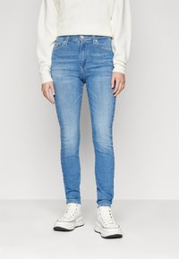 Jeans skinny de mezclilla de color azul claro con una cintura alta, cinco bolsillos y un ligero desgaste, combinados con zapatillas blancas gruesas.