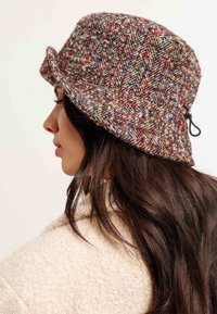 Cappello a secchiello di lana multicolore con motivo a zig-zag, dotato di un bordo flessibile e di un cordino regolabile sul lato.