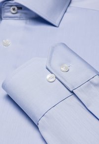 Lichtblauw overhemd van zachte stof, met een puntcollar en dubbele knopmanchetten. Voorzien van witte plastic knopen en fijne diagonale strepen.