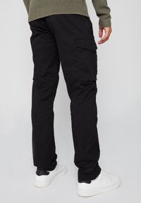 Zwarte cargobroek van katoen, met zijzakken en een recht model. G gedragen met witte sneakers.