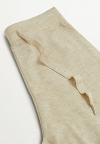 Tessuto a maglia elasticizzato beige con una superficie liscia. Presenta una cintura piatta e un'anello decorativo con una piccola punta metallica.