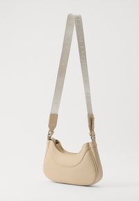 Borsa a mano in pelle beige con una texture liscia, forma curva e tracolla regolabile con logo del brand in rilievo. Chiusura con zip sulla parte superiore.