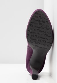 Chaussure en daim violet avec un bout pointu et une fermeture éclair latérale. La semelle en caoutchouc noir présente le nom de la marque "Tamaris" en relief ainsi que la taille 37.