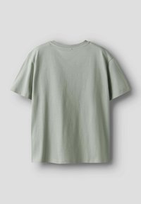 Camiseta de manga corta en suave algodón de color verde claro. Cuello redondeado, corte holgado, textura suave y detalles mínimos en la parte posterior.