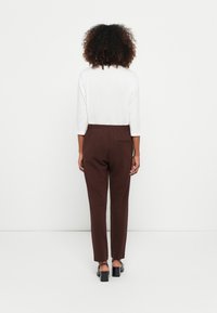 Brown tapered trousers with an elastic waistband and back pocket, paired with a white 3/4 sleeve top. Smooth fabric and minimal design.