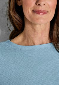 Helles blauer Strickpullover mit weit ausgeschnittenem Hals, aus strukturiertem Stoff mit glatter Oberfläche. Haare und Haut sind im Bild sichtbar.