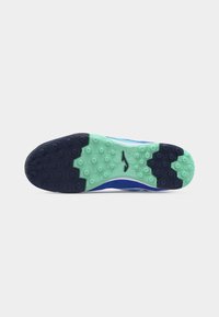Semelle d'une chaussure de sport bleue avec un motif hexagonal noir et vert et un logo central sur un fond blanc uni.