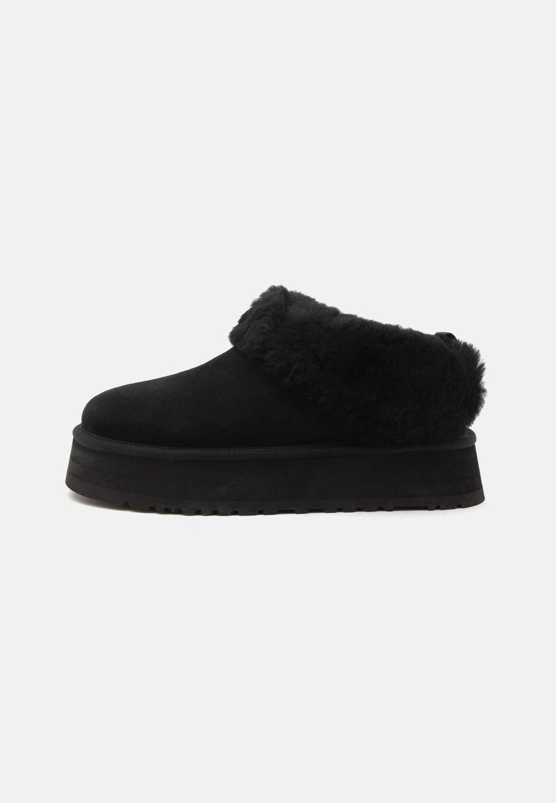 Chaussure plateforme noire à enfiler avec semelle épaisse et matelassée, et col en fourrure duveteuse autour de l’ouverture.