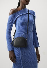 Abito a maglia blu a coste con design off-shoulder, caratterizzato da dettagli con bottoni. Piccola borsa a tracolla nera in pelle con logo impresso.