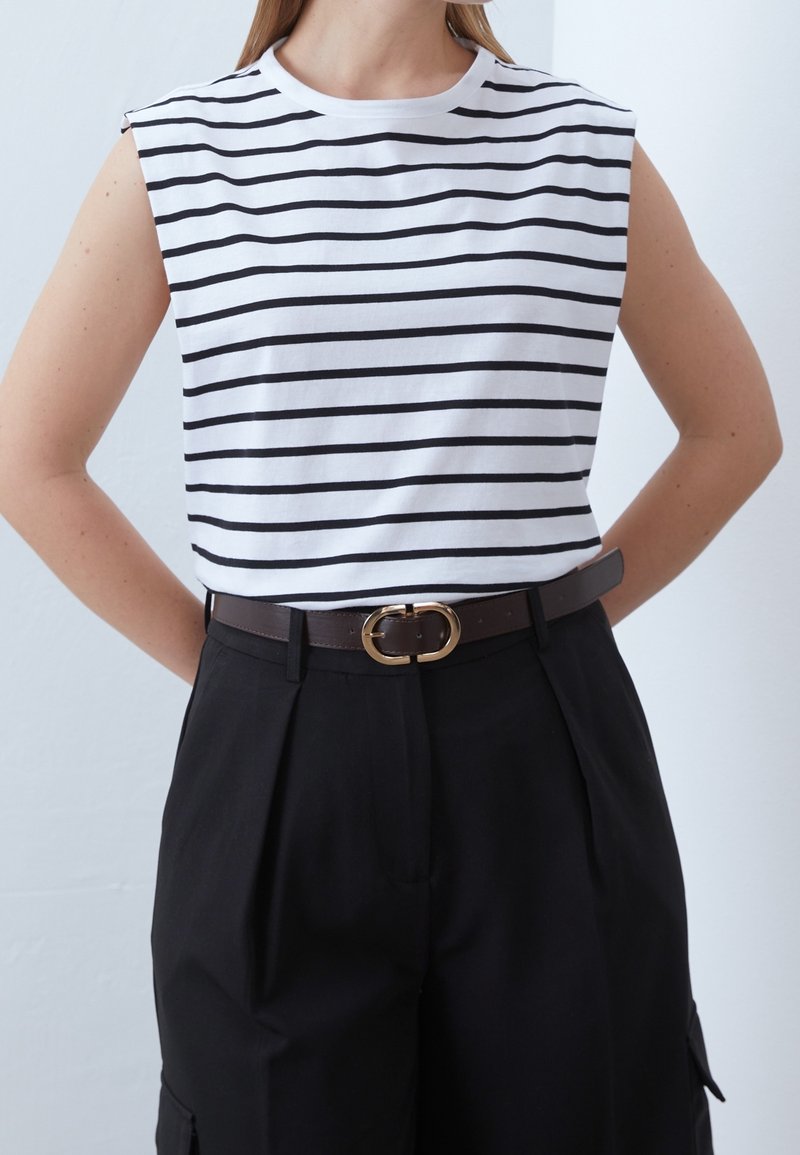 Haut sans manches blanc avec des rayures horizontales noires, associé à un pantalon noir taille haute et une ceinture marron avec une boucle ovale en or.