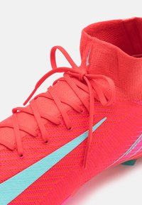 Bright pink soccer shoe with a knit upper, featuring tonal laces, a light blue swoosh, and a snug ankle collar for support.