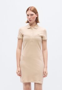 Μπεζ φόρεμα πόλο από απαλό ύφασμα, με γιακά, κουμπότρυπα, κοντά μανίκια και μικρό λογότυπο στο στήθος.