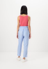 Top sin mangas de color rosa combinado con pantalones de cintura elástica de color azul claro. Los pantalones tienen un corte relajado y bolsillos, con un dobladillo limpio.