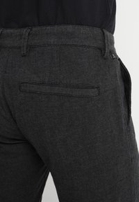 Black textured trousers with a subtle pattern, featuring a back pocket and a fitted waistband. Durable fabric suitable for casual wear.