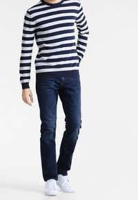 Mörkblå och grårandig tröja för män med rund hals, i kombination med mörkblå jeans och vita sneakers, vilket ger en avslappnad look.