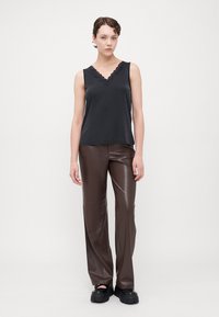 Top negru fără mâneci, cu decolteu în V evazat, asortat cu pantaloni din piele ecologică maro, cu talie înaltă, și pantofi chunky negri cu platforme.