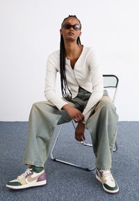 Bijela rebrasta zip-pulover, svijetloplave široke traperice i višebojne Nike tenisice s akcentima zelene, ljubičaste i bež boje. Nosene crne sunčane naočale.