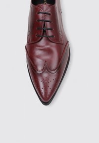 Zapato de vestir de cuero burdeos con punta afilada, detalles perforados y un acabado suave y elegante. Presenta cordones negros y costuras sutiles.